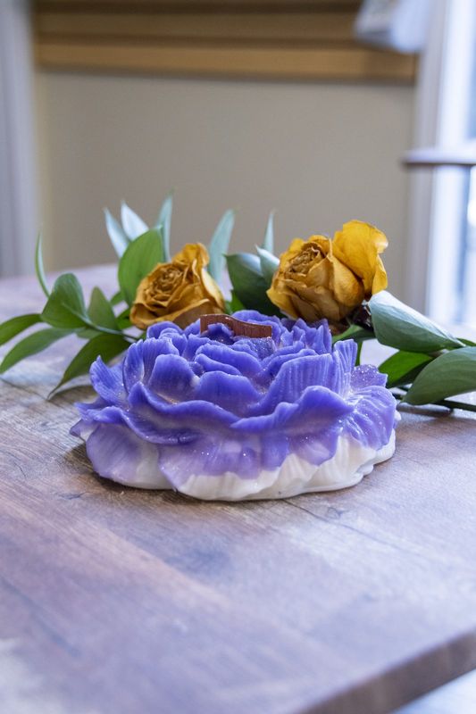 A violet peony candle with fresh roses